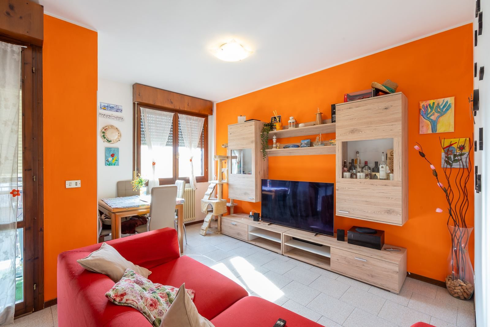 Soggiorno luminoso con divano rosso e parete arancione